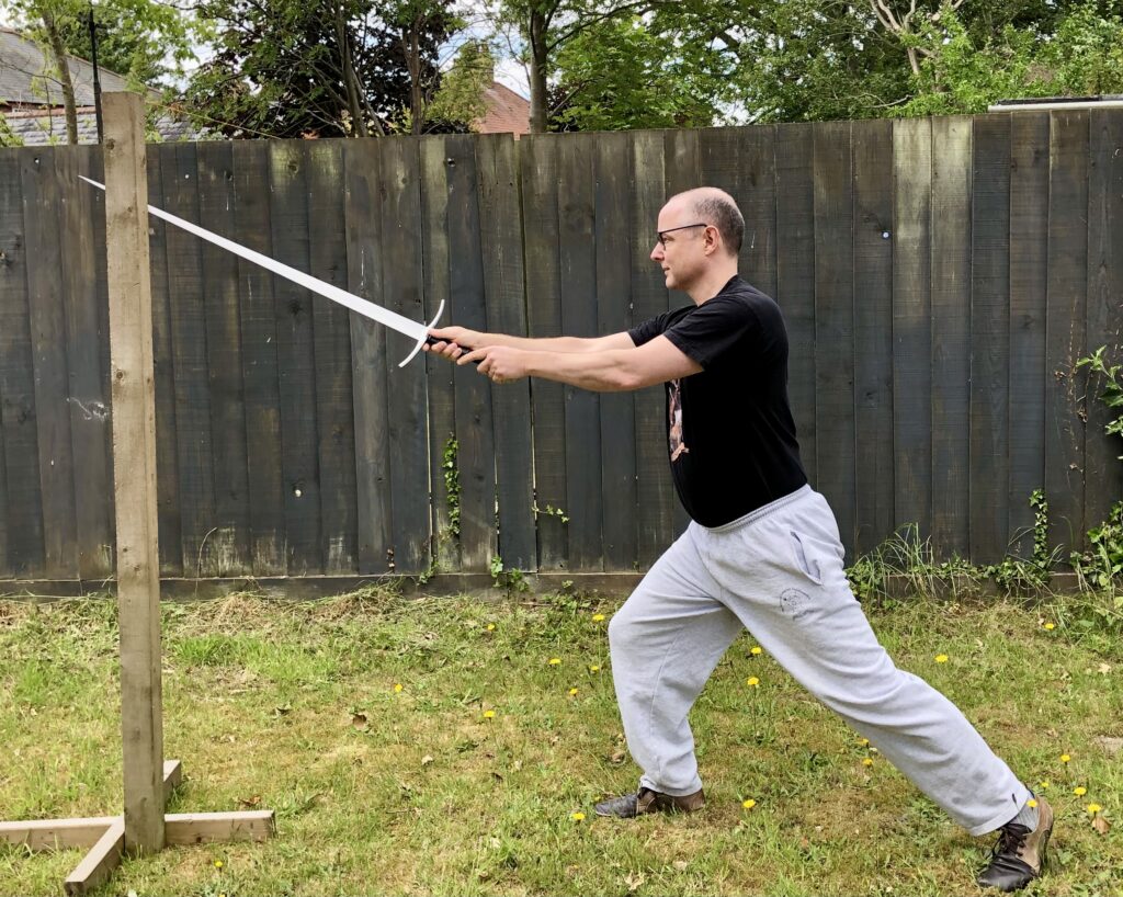 Guy Windsor striking at a pell with a longsword, entering the fray